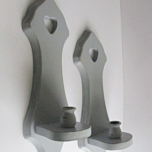 May include: Two gray wooden wall sconces with heart-shaped cutouts and candle holders.