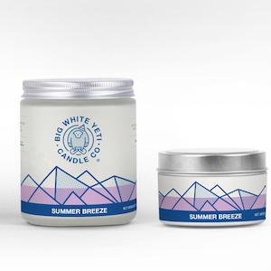 May include: Two silver candle jars with white labels. The labels feature a blue and white logo with a yeti wearing a hat and the text "Big White Yeti Candle Co.". The jars are labeled "Summer Breeze" and feature a graphic of blue and purple mountains.