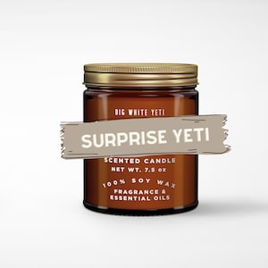 May include: A brown glass candle jar with a gold lid. The label reads "BIG WHITE YETI" and "SURPRISE YETI". The candle is scented and made with 100% soy wax, fragrance, and essential oils. The net weight is 7.5 ounces.