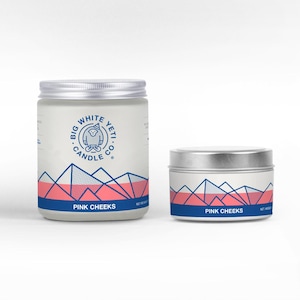 May include: Two candles with a white background and a blue and pink mountain design. The larger candle has the text "Big White Yeti Candle Co." and "Pink Cheeks". The smaller candle has the text "Pink Cheeks".