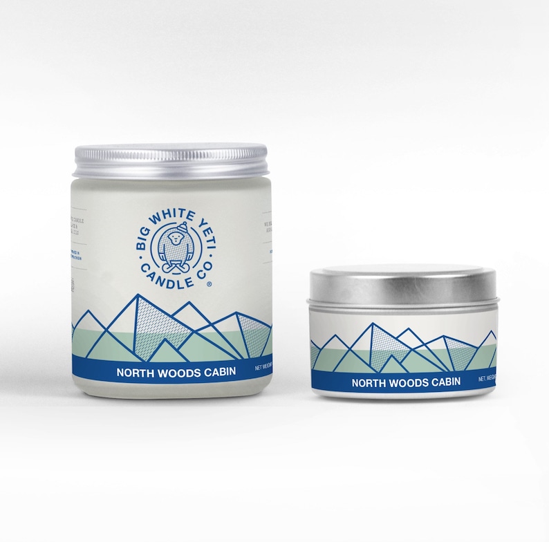 Pu&ograve; includere: Due candele con un'etichetta bianca e un design di montagna blu e verde. L'etichetta dice "Big White Yeti Candle Co." e "North Woods Cabin".