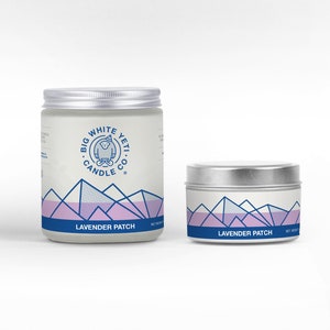 May include: Two candles in glass jars with silver lids. The jars have a white background with a blue and white logo that says "Big White Yeti Candle Co." and a graphic of a yeti. The jars have a purple and white mountain range design and the text "Lavender Patch".