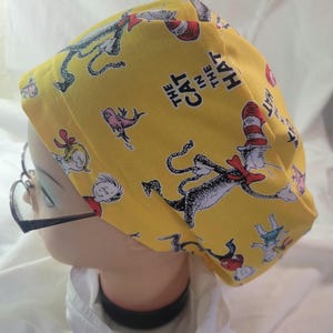 Peut inclure: Bonnet de chirurgien jaune avec des illustrations de personnages du livre "Le Chat chapeauté". Le bonnet présente le Chat chapeauté, les Choses 1 et 2, et d'autres personnages. Le texte "The Cat in the Hat" est également visible.