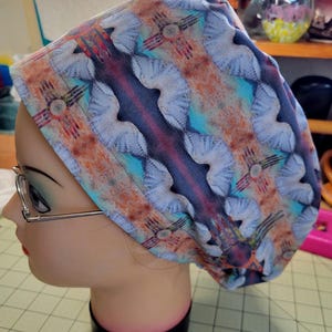 Peut inclure: Un bonnet chirurgical coloré avec un motif sud-ouest, turquoise, orange et blanc. Le bonnet a un symbole "Zia" dessus.