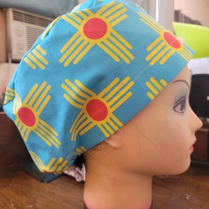 May include: A blue scrub hat with a yellow and red Zia symbol pattern. The hat is made of a soft, comfortable fabric and is perfect for nurses, doctors, and other healthcare professionals.