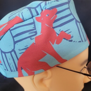 May include: A blue and red patterned fabric hat with a red animal design. The hat is worn on a mannequin head.