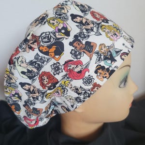 Peut inclure: Un bonnet de travail blanc avec un motif de princesses Disney avec des tatouages et des fleurs. Les princesses portent des vêtements noirs et ont des cheveux colorés.