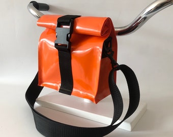 May include: Orange and black crossbody bag with a buckle closure and adjustable strap. The bag is made of a shiny, waterproof material.