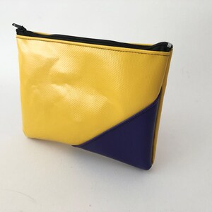 May include: A yellow and blue zipped pouch. The pouch is mainly yellow with a textured surface and a dark blue triangular accent on the corner. The zip is black.