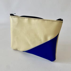 Puede incluir: Una pequeña bolsa con cremallera de color crema con una sección triangular azul en la parte inferior.
