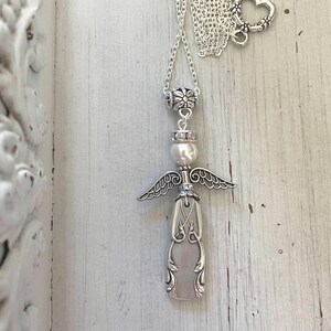 Peut inclure: Un collier argent&eacute; avec un pendentif en forme d'ange. Le pendentif est compos&eacute; d'un manche en m&eacute;tal d&eacute;coratif, d'une perle blanche en guise de t&ecirc;te et d'ailes en m&eacute;tal argent&eacute;. Le collier comprend une cha&icirc;ne argent&eacute;e avec un fermoir en c&oelig;ur.
