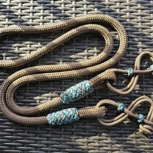 May include: A brown and blue rope halter and lead rope set. The rope is a braided design with blue accents. The halter has two loops and the lead rope has a braided section in the middle. The set is designed for equestrian use.
