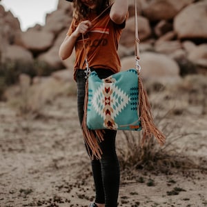 May include: A turquoise and brown patterned crossbody bag with fringe. The bag has a geometric design with white, red, and yellow accents.