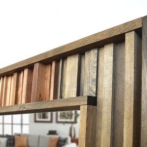 Puede incluir: Un espejo rectangular con un marco &uacute;nico hecho de diferentes tonos de madera. El marco est&aacute; hecho de finas tiras de madera dispuestas en un patr&oacute;n vertical, creando un efecto de capas. El espejo est&aacute; rodeado por un borde grueso de madera marr&oacute;n oscuro.