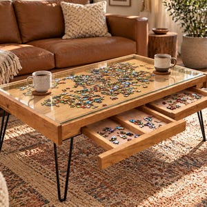 May include: A rectangular wooden coffee table with a glass top surface containing a partially assembled jigsaw puzzle. The table features four black metal hairpin legs and two pull-out drawers underneath, each holding additional puzzle pieces.