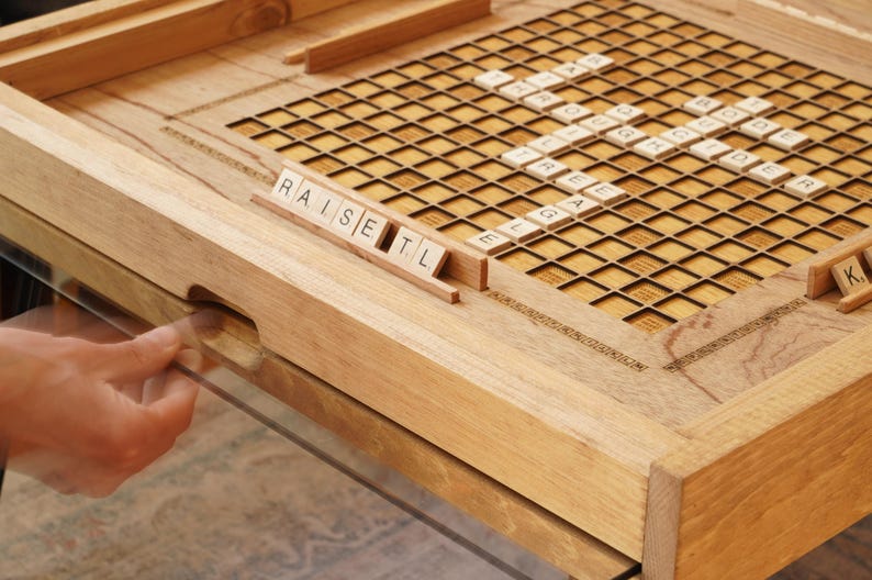 K&ouml;nnte beinhalten: Ein h&ouml;lzernes Spielbrett mit einem Gitter aus Quadraten und Buchstabenpl&auml;ttchen, die die W&ouml;rter "raise", "set" und "tl" buchstabieren.