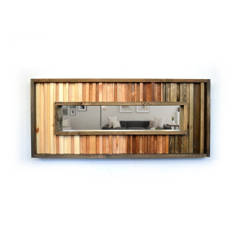 Puede incluir: Un espejo rectangular con un marco de madera hecho de varios tonos de madera marr&oacute;n. El marco est&aacute; hecho de finas tiras de madera dispuestas verticalmente. El espejo refleja una habitaci&oacute;n con un sof&aacute; y otros muebles.