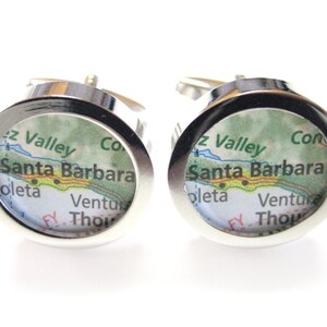 May include: A pair of silver cufflinks with a map of Santa Barbara, California inside. The map shows the Santa Barbara Channel, the Santa Ynez Valley, and the cities of Goleta and Ventura.