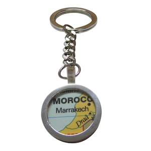May include: Silver keychain with a round, silver-rimmed charm featuring a map of Morocco with the text "MOROCCO" and "Marrakech" printed on it.