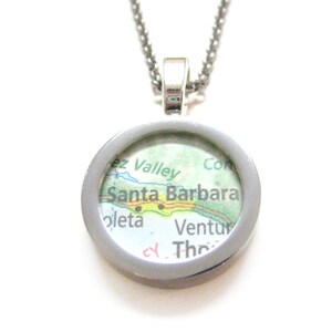 May include: A silver necklace with a round pendant featuring a map of Santa Barbara, California. The map is in shades of green, blue, and yellow, with the city name clearly visible.