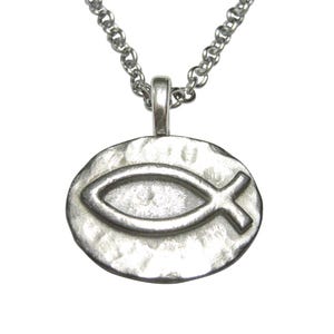 Puede incluir: Un collar de plata con un colgante ovalado martillado que presenta un símbolo de pez estilizado.