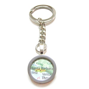 May include: Silver keychain with a round map of Santa Barbara, California. The map shows the city and surrounding areas, including the Santa Ynez Valley, Goleta, and Ventura.