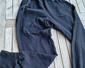 Puede incluir: Pantalón negro de algodón con cintura ancha y piernas con puños. El pantalón tiene una textura de tejido de waffle y está doblado sobre una superficie de madera.