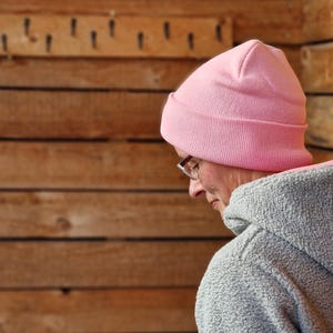 May include: A person wearing a pink beanie and a gray fleece jacket. The person is looking down and has glasses on.