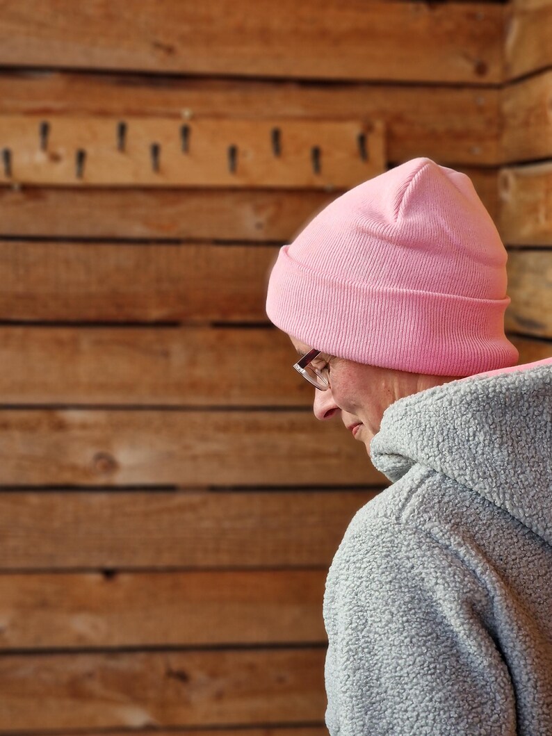 May include: A person wearing a pink beanie and a gray fleece jacket. The person is looking down and has glasses on.