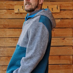 May include: A gray and teal hooded sweatshirt with a zipper closure. The sweatshirt has a contrasting teal panel on the left side and a teal panel on the right shoulder.