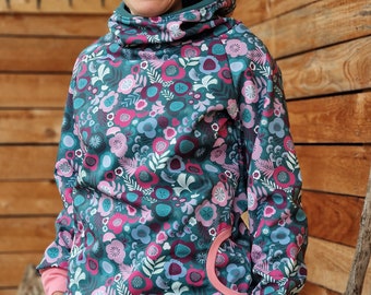 May include: A teal hoodie with a floral pattern in pink, blue, and white. The hoodie has a high collar, a kangaroo pocket with a pink trim, and pink cuffs. The person is wearing gray jeans and glasses.