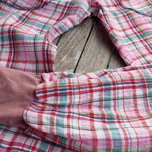 May include: Pink, red, green, and white plaid pants with a mauve waistband and cuffs. The pants are made of a lightweight fabric and appear to be handmade. The fabric has a soft, slightly wrinkled texture.