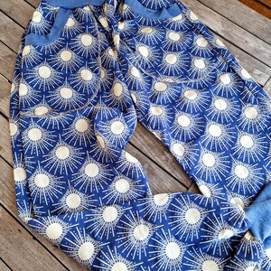 Puede incluir: Pantalones azules y blancos con estampado, con una cintura elástica ancha y dos bolsillos. El estampado presenta rayos de sol blancos sobre un fondo azul.