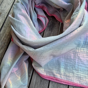 May include: A light gray scarf with a pink iridescent pattern and a pink stitched edge.