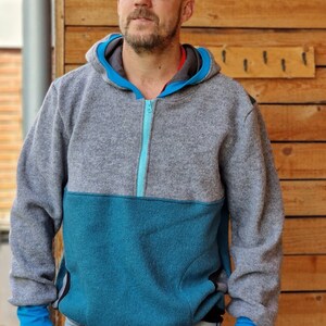 May include: A gray and teal hooded sweatshirt with a zipper closure. The sweatshirt has a contrasting teal panel on the lower half and teal zipper trim.