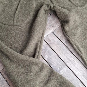 Puede incluir: Pantalones verde oliva con cintura alta turquesa y ribete de bolsillo a juego. Los pantalones están hechos de una tela suave y texturizada y están sobre una superficie de madera.