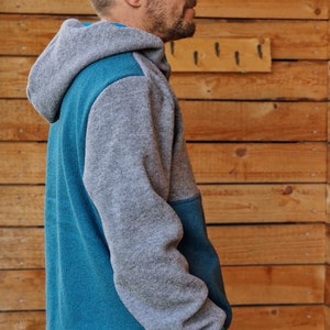 May include: A gray and teal hooded sweatshirt with a zipper closure. The sweatshirt has a contrasting color panel on the front and sleeves.