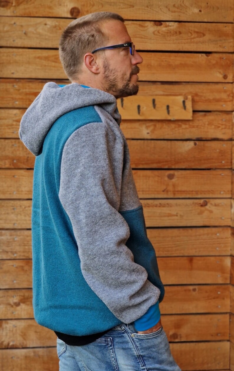 May include: A gray and teal hooded sweatshirt with a zipper closure. The sweatshirt has a contrasting color panel on the front and sleeves.