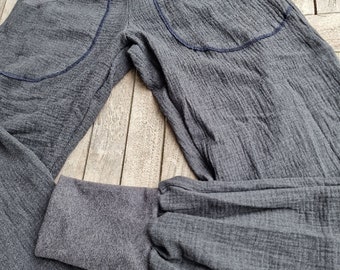 May include: Gray cotton pants with a wide leg and a gathered elastic waistband. The pants have two large pockets on the back with blue stitching.