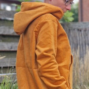May include: A mustard yellow corduroy hooded jacket featuring a textured ribbed fabric, long sleeves with light green cuffs, and a straight hemline. The jacket has a structured hood and a solid color design, providing a casual outer layer.