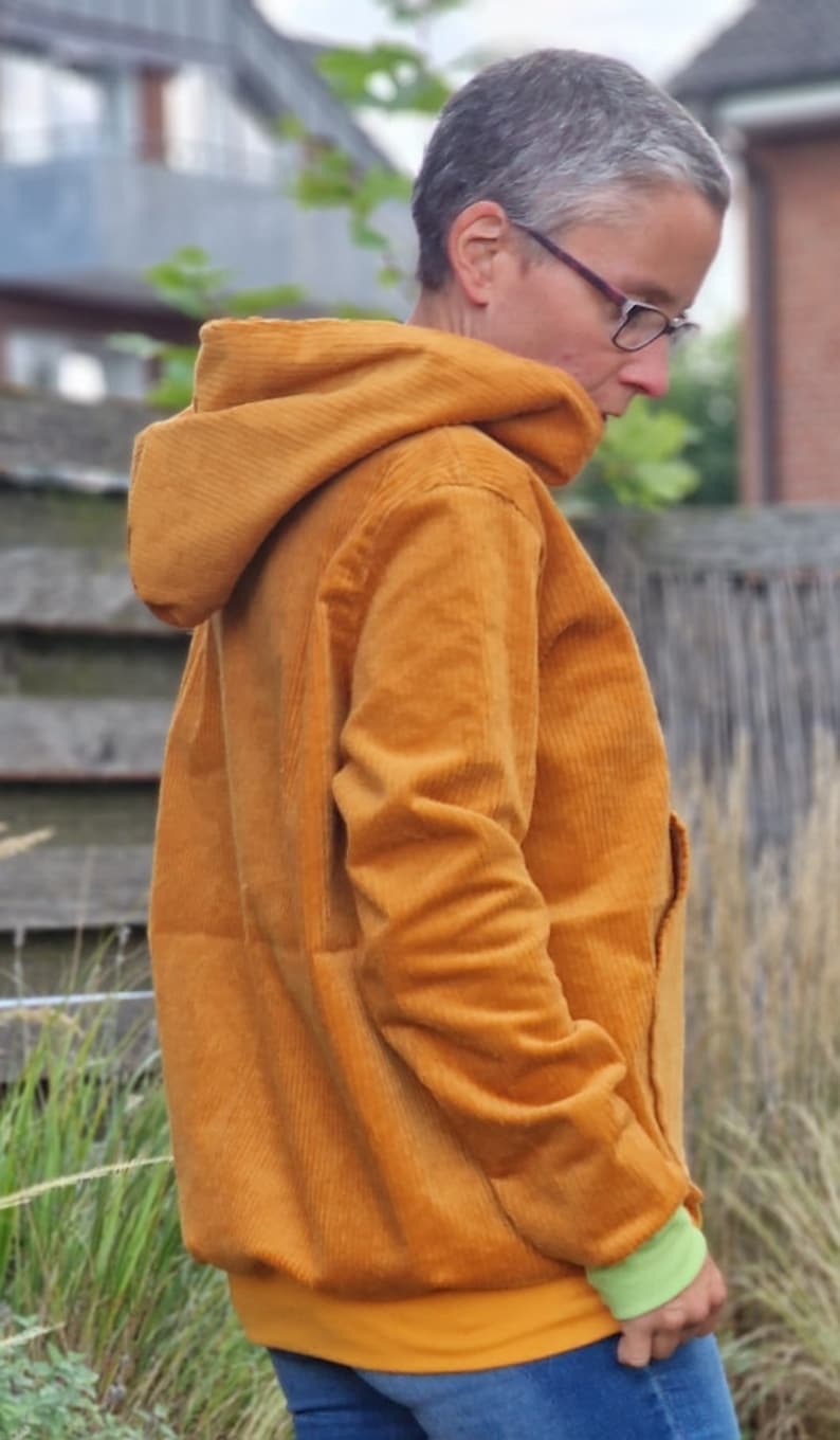 May include: A mustard yellow corduroy hooded jacket featuring a textured ribbed fabric, long sleeves with light green cuffs, and a straight hemline. The jacket has a structured hood and a solid color design, providing a casual outer layer.