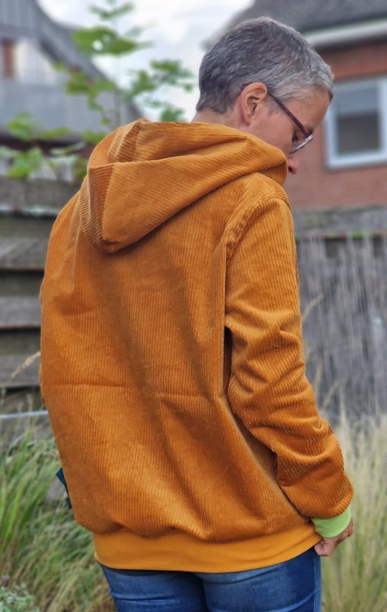 May include: A mustard yellow corduroy hooded sweatshirt featuring a textured ribbed fabric, long sleeves, and a solid mustard yellow hem. The garment includes a hood and is worn over a light green undershirt and blue denim jeans.