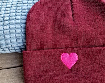 May include: A maroon beanie with a pink heart embroidered on the front.