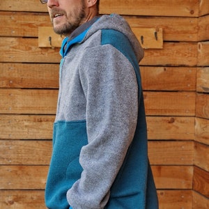 May include: A gray and teal hooded sweatshirt with a zipper closure. The sweatshirt has a contrasting teal panel on the front and sleeves.