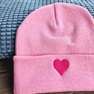 May include: Pink knit beanie with a red heart embroidered on the front.