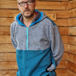 May include: A gray and teal hooded sweatshirt with a zipper closure. The sweatshirt has a contrasting teal panel on the lower half and a black pocket on the right side.