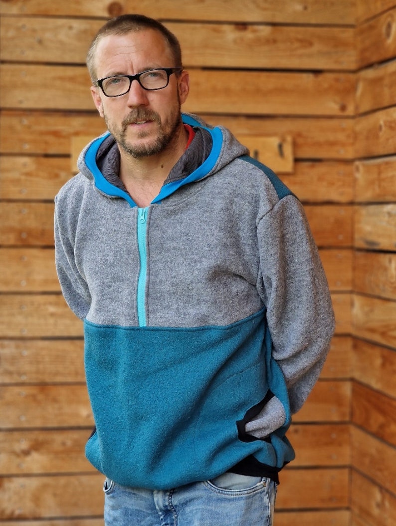 May include: A gray and teal hooded sweatshirt with a zipper closure. The sweatshirt has a contrasting teal panel on the lower half and a black pocket on the right side.