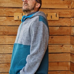 May include: A gray and teal fleece hoodie with a zipper closure. The hoodie has a hood and a pocket on the front.