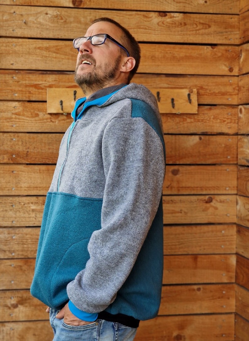 May include: A gray and teal fleece hoodie with a zipper closure. The hoodie has a hood and a pocket on the front.