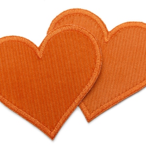 Könnte beinhalten: Zwei orangefarbene Filz-Herzen mit einem gestickten Rand.